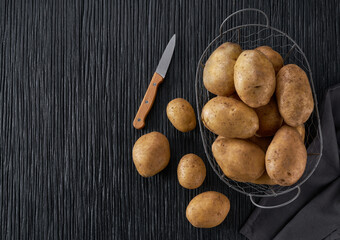 Fresh potato tubers on a black wooden table, top view.
