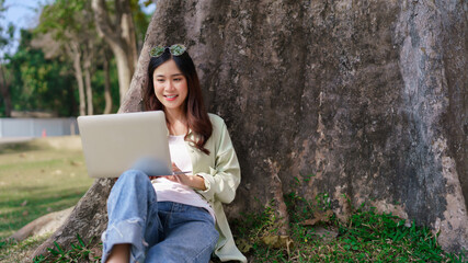 Women leaning on the tree to working and surfing social media on laptop while relaxation in park