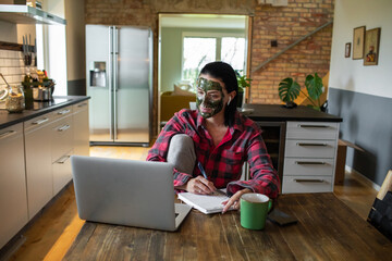 Young adult woman working on her laptop in the kitchen of her home