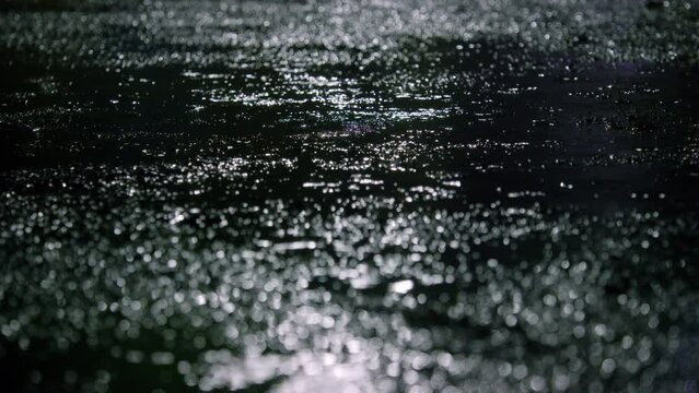 Closeup of rain drops falling on puddle with lights reflection on city sidewalk, Rain drop with street lights at night, Weather or environment