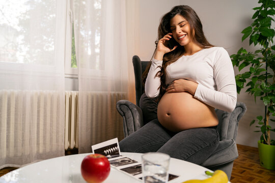Young happy pregnant woman looking ultra sound images and sex of the baby and calling somebody on the phone
