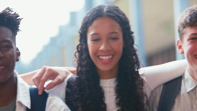 Camera tracks along faces of class of high school students sitting on wall outside and smiling at camera - shot in slow motion