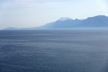 Beautiful mediterranean landscape in soft colors with calm sea and high mountains silhouettes covered with light haze on skyline
