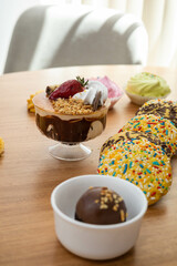 table served with delicious desserts among them cup with ice cream, cream and strawberry, congeeous cookies, and chocolate ball, appetizing sweet food in studio