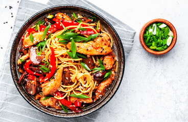 Stir fry noodles with chicken, red paprika, mushrooms, chives and sesame seeds in bowl. Asian cuisine dish. White table background, top view