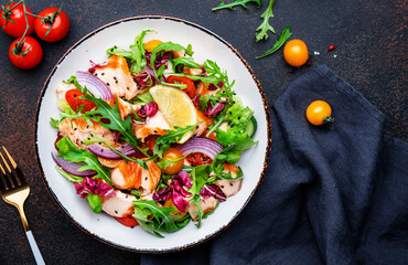 Gourmet salad with grilled salmon with tomatoes, cucumber, arugula, radicchio, red onion and lettuce with lemon oil dressing. Healthy lunch. Brown stone table background, top view