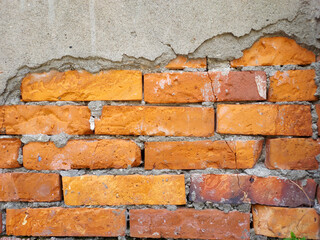 Damaged concrete wall with red bricks exposed.
