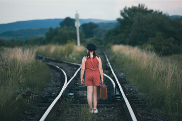 Fototapeta premium A little girl in a dress walking on an abandoned railroad tracks.