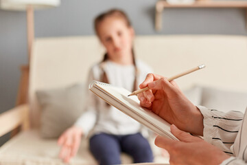 Female child having session with psychologist who takes notes on her emotional and mental state, carefully listening to the girl's concerns and issues.