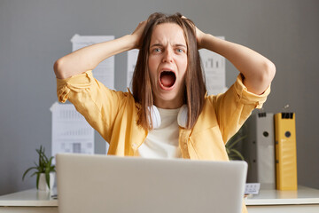 Young woman freelancer looked frustrated and aggressive working online on laptop in her home office, has dissatisfied and irritated expression, screaming with frustration and anger.