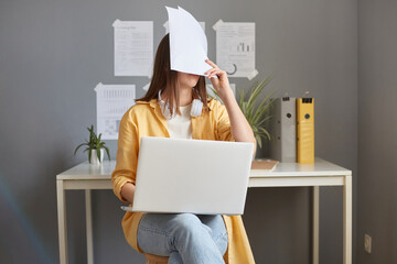 Tired exhausted woman working with documents and laptop having job troubles covering face with...