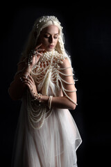 Close up portrait of beautiful blonde female model wearing an extravagant pearl jewelled gown. Gestural arms reaching out,  isolated on a black studio background.