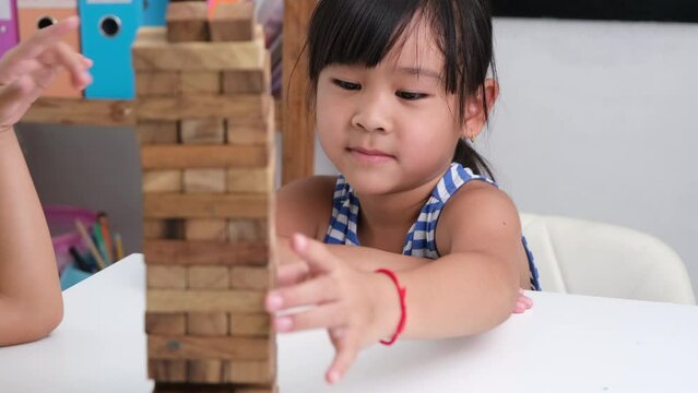 Cute Asian siblings having fun playing Jenga together. Two children playing Jenga board game on table in room at home. Wooden puzzles are games that increase intelligence for children.