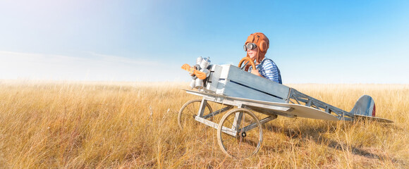 Little boy is playing the plane.
Happy and funy child imagines himself an aircraft pilot and plays in a aviator costume in an open-air field against a blue sky on a summer sunny day.  - 600642147