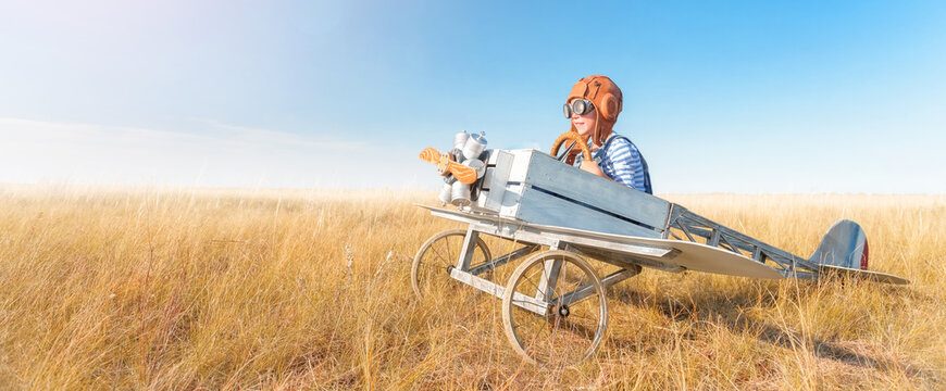 Little boy is playing the plane.
Happy and funy child imagines himself an aircraft pilot and plays in a aviator costume in an open-air field against a blue sky on a summer sunny day. 