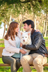 Fototapeta premium Young caucasian couple hugging with their dog sitting on a bench.
