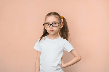 Portrait of a girl of elementary school age in rectangular optical glasses on a pink background.