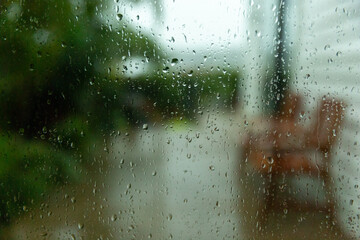 Rainy day. Windowpane covered in raindrops, with a view of a backyard garden visible behind it. Raindrops create a blurry effect on the view. Focus on the foreground.