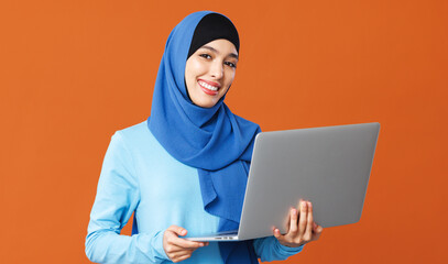 beautiful muslim woman smiling and holding  laptop in her hands on orange background