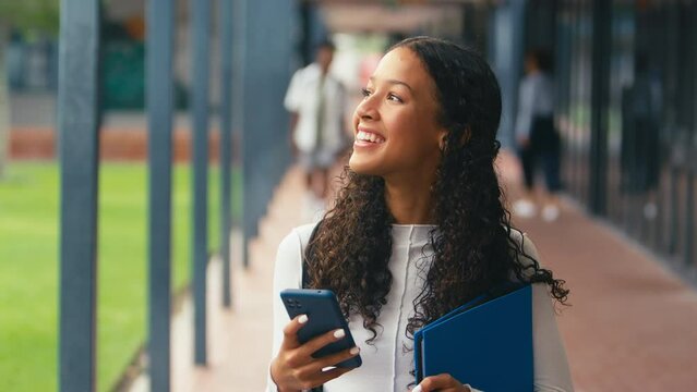 Female high school student walking outside classrooms checking social media or internet on mobile phone - shot in slow motion