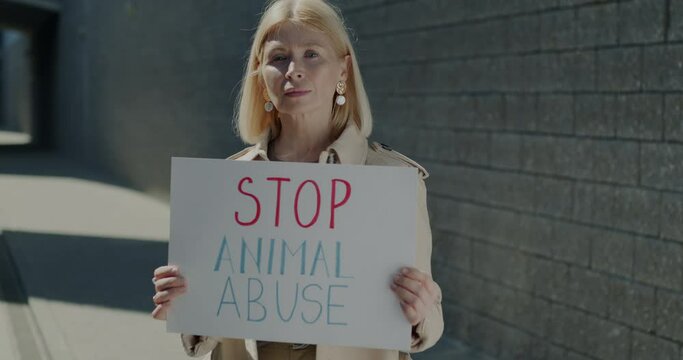 Portrait of mature woman holding Stop Aminal Abuse sign protecting wildlife standing against urban background. Vegan lifestyle and awareness concept.