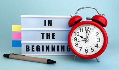 Text In the beginning written on the lightbox with alarm clock and colorfull stickers on blue background