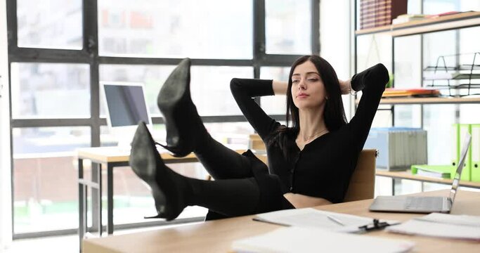 Happy positive calm business woman employee is resting and taking break at work. Manager keeps hand behind head and sits at office desk