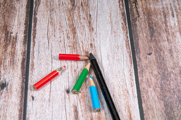 Pencil in black with small worn crayons on wooden background