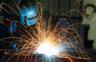 Industrial workers at steel structure welding plant A welder is welding metal parts in a small...