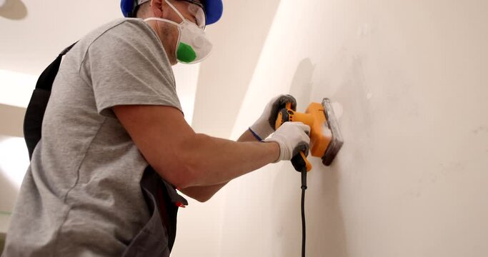 Craftsman sands gray plastered wall with special manual machine with emery net. Repairman removing putty defects in the process of finishing work