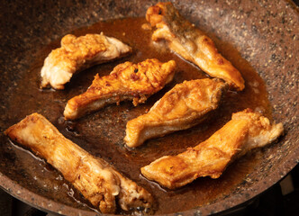 The fish is fried in a frying pan in oil. Close-up.