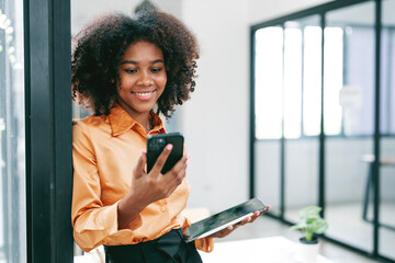 Young smiley black woman using mobile phone standing in office.