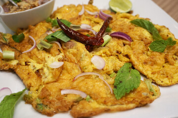Fired egg or omelet street food menu with spicy and vegetable in white dish.
