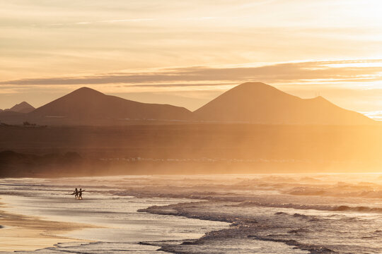 surfers coming out of the water at sunset