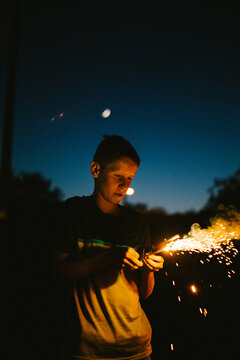 Boy holds a fire sparkler on July 4th in the dark in summer