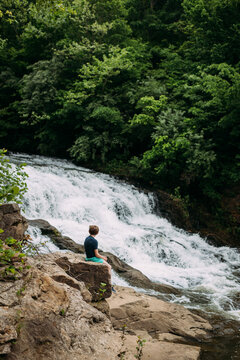 Person sitting on rocks admiring waterfall