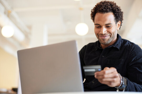 Smiling businessman holding credit card by laptop in office
