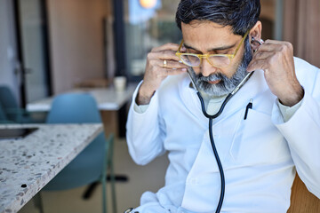 Mature male doctor adjusting stethoscope in clinic