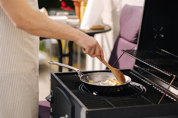 Middle selection of human hands stirs with a wooden spoon food on frying pan. BBQ grill outdoor on fresh air