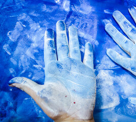 Children's hands with white paint on a blue picturesque background. - 600667751