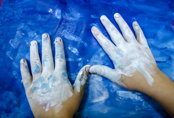 Children's hands with white paint on a blue picturesque background. - 600667754