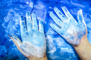 Children's hands with white paint on a blue picturesque background. - 600667763