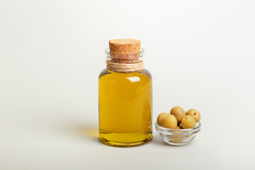 Horizontal picture of olive oil in small glass bottle and whole green olives in small glass transparent bowl in light background.