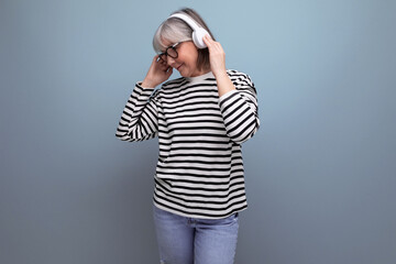 stylish modern 60s old lady listens to music in headphones and dances on a bright background with copy space