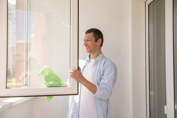 Fototapeta premium Happy man is cleaning the house. Wash windows with a rag on the balcony