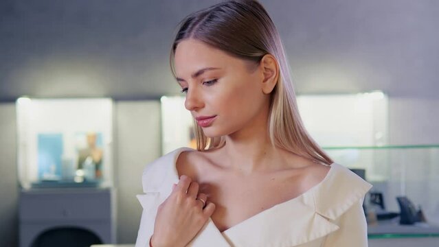 Pretty graceful girl with a beautiful face and a diamond gold ring posing in a jewelry store with accessories. Positive blonde girl in a white jacket is trying on a wedding ring. Jewelry advertising.