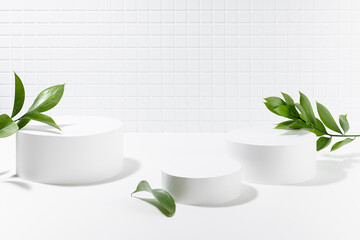 Summer abstract white stage, three round podiums mockup for presentation cosmetic products, goods, advertising, in light interior, tiny mosaic tile, fresh tropical green leaves in sunbeam, shadow.