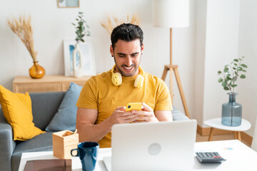 Young man sitting at desk at home using mobile phone.