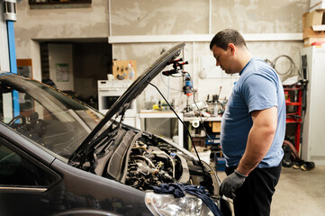 An auto mechanic looks under the hood of a car in a garage. repairing a car and inspecting a broken engine. manual diagnostics. machine maintenance