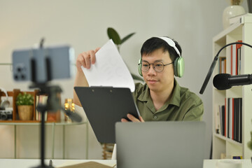 Asian male radio host using condenser microphone recording or streaming podcast from home studio